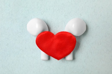 Modern earphones and red heart on turquoise background, flat lay. Listening love music songs