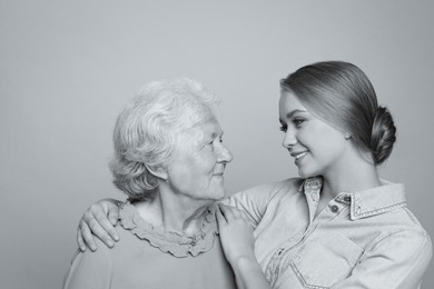 Young woman and her grandmother on light background. Black and white photography