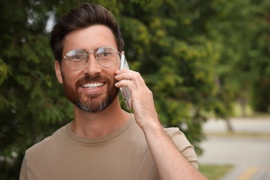 Smiling bearded man talking on phone outdoors. Space for text
