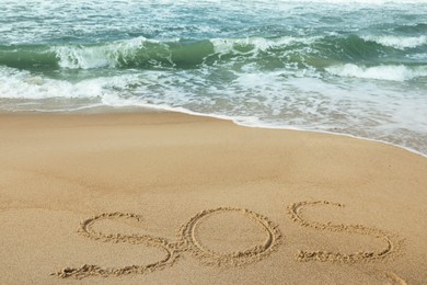 Message SOS drawn on sand near wavy sea