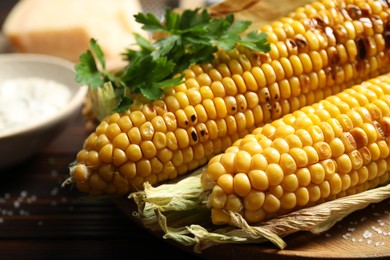 Photo of Delicious grilled sweet corn cobs on board, closeup