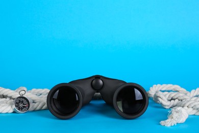 Modern binoculars, compass and rope on light blue background, space for text