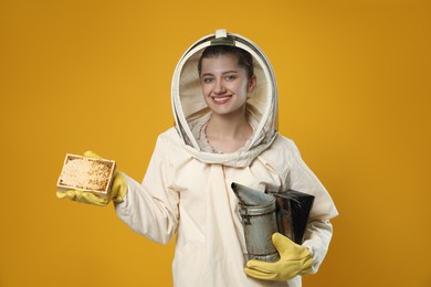 Photo of Beekeeper in uniform holding smokepot and hive frame with honeycomb on yellow background