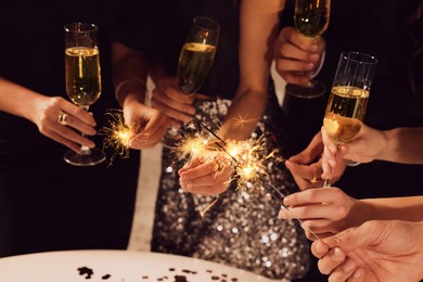 Friends with glasses of sparkling wine and sparklers celebrating New Year, closeup