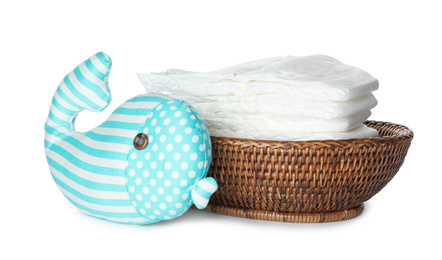 Wicker bowl with disposable diapers and toy on white background
