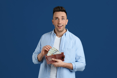 Happy man with cash money and wallet on blue background
