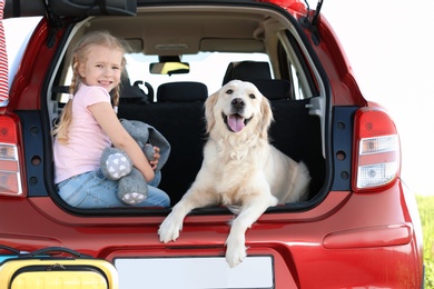 Photo of Cute little girl and her dog in open car trunk