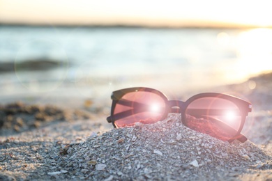 Stylish sunglasses on sandy beach at sunset
