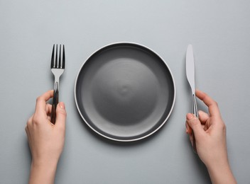 Photo of Woman with empty plate and cutlery on light grey background, top view