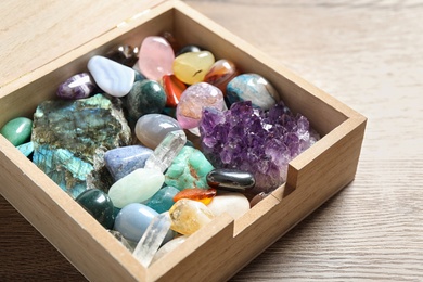 Photo of Box with different beautiful gemstones on wooden table