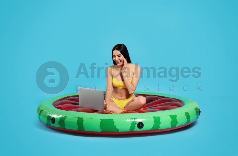 Young woman using laptop while sitting on inflatable mattress against light blue background