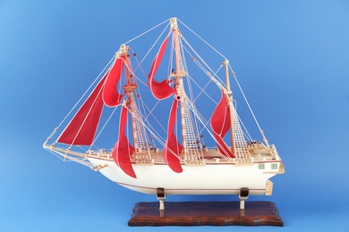 Miniature model of old ship with red sails on blue background