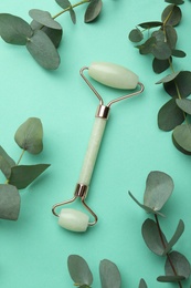 Natural face roller and eucalyptus on turquoise background, flat lay