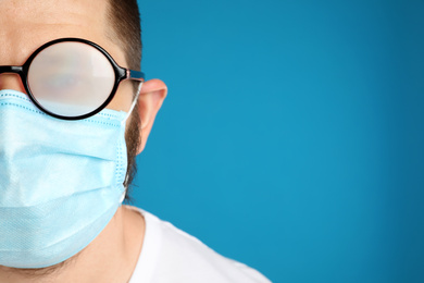 Man with foggy glasses caused by wearing disposable mask on blue background, space for text. Protective measure during coronavirus pandemic