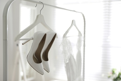 Pair of white high heel shoes and wedding dress on clothing rack indoors. Space for text