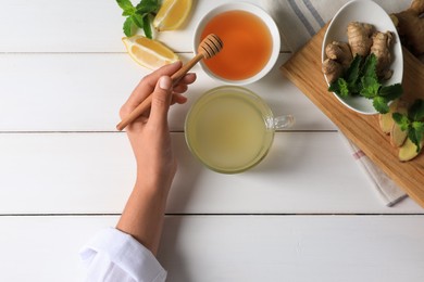 Photo of Woman drinking delicious ginger tea with honey at white wooden table, top view