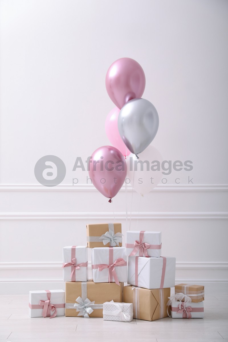 Many gift boxes and balloons near white wall in room