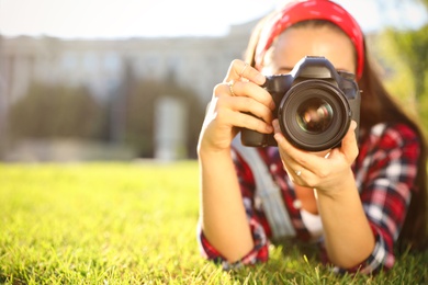 Young photographer taking picture with professional camera on green grass. Space for text