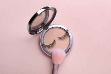 False eyelashes and face powder with brush on pink background, flat lay