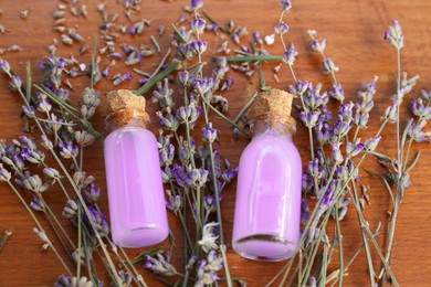 Beautiful lavender flowers and bottles with essence oil on wooden table, closeup