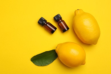 Bottles of citrus essential oil and fresh lemons on yellow background, flat lay