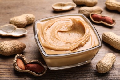 Photo of Yummy peanut butter in glass bowl on wooden table, closeup