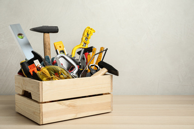 Crate with different carpenter's tools on wooden table. Space for text