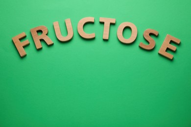 Photo of Word Fructose made of wooden letters on green background, flat lay. Space for text