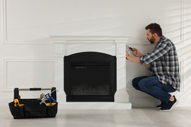 Man with screwdriver installing electric fireplace in room