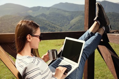 Young woman working with laptop on outdoor wooden terrace in mountains