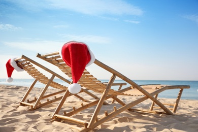 Photo of Sun loungers with Santa's hats on beach. Christmas vacation