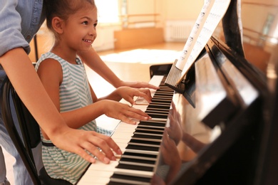 Young woman teaching little girl to play piano indoors