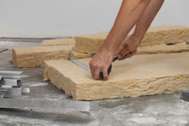 Worker measuring and cutting insulation material indoors, closeup