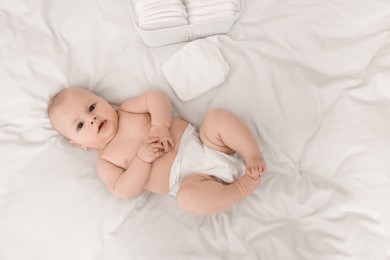 Photo of Cute baby and diapers on white bed, top view