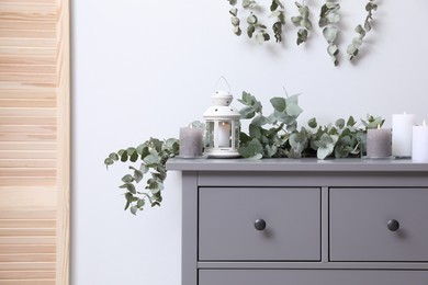 Stylish chest of drawers decorated with beautiful eucalyptus garland and candles indoors