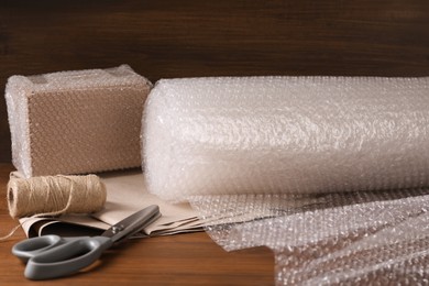 Scissors, twine, paper, roll of bubble wrap and packed box on wooden table