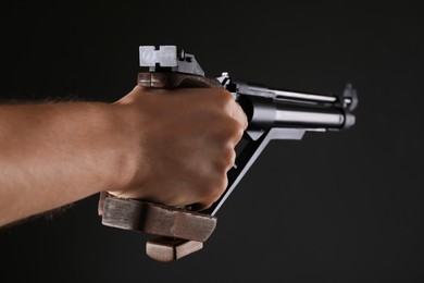Photo of Gun shooting sport. Man aiming standard pistol on dark background, closeup