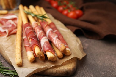 Photo of Delicious grissini sticks with prosciutto on brown table, closeup. Space for text