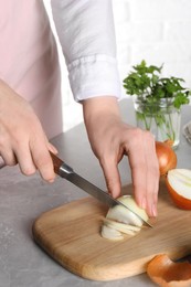 Photo of Woman cutting ripe onion at grey textured table, closeup