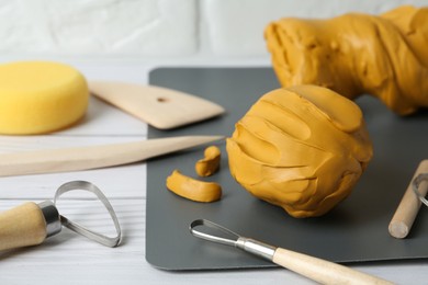 Clay and set of modeling tools on white wooden table, closeup