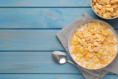 Bowl of tasty corn flakes served on light blue wooden table, flat lay. Space for text