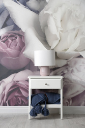 White nightstand near wall with floral wallpaper. Stylish room interior