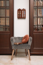 Comfortable armchair with pillow and book between wooden bookcases in library