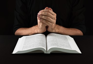 Man with Bible praying at black table, closeup
