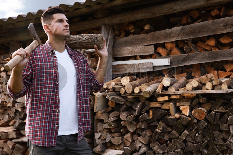 Man with ax and log near wood pile outdoors