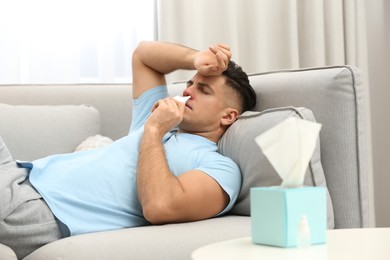 Ill man using nasal spray on sofa at home