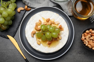Brie cheese served with grape, cashew nuts and honey on dark grey table, flat lay