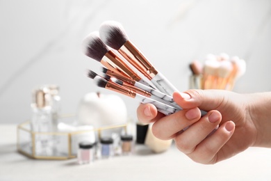 Woman holding set of makeup brushes on blurred background, closeup