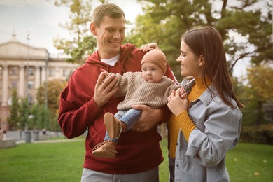 Happy parents with their adorable baby walking in park