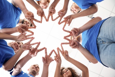 Team of volunteers putting their hands together on light background, bottom view